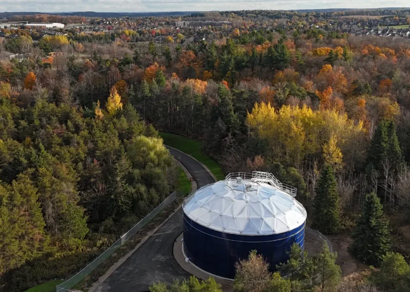 A Greatario built water tower sits in the foreground surrounded by autumn trees, in the distance is a small town.