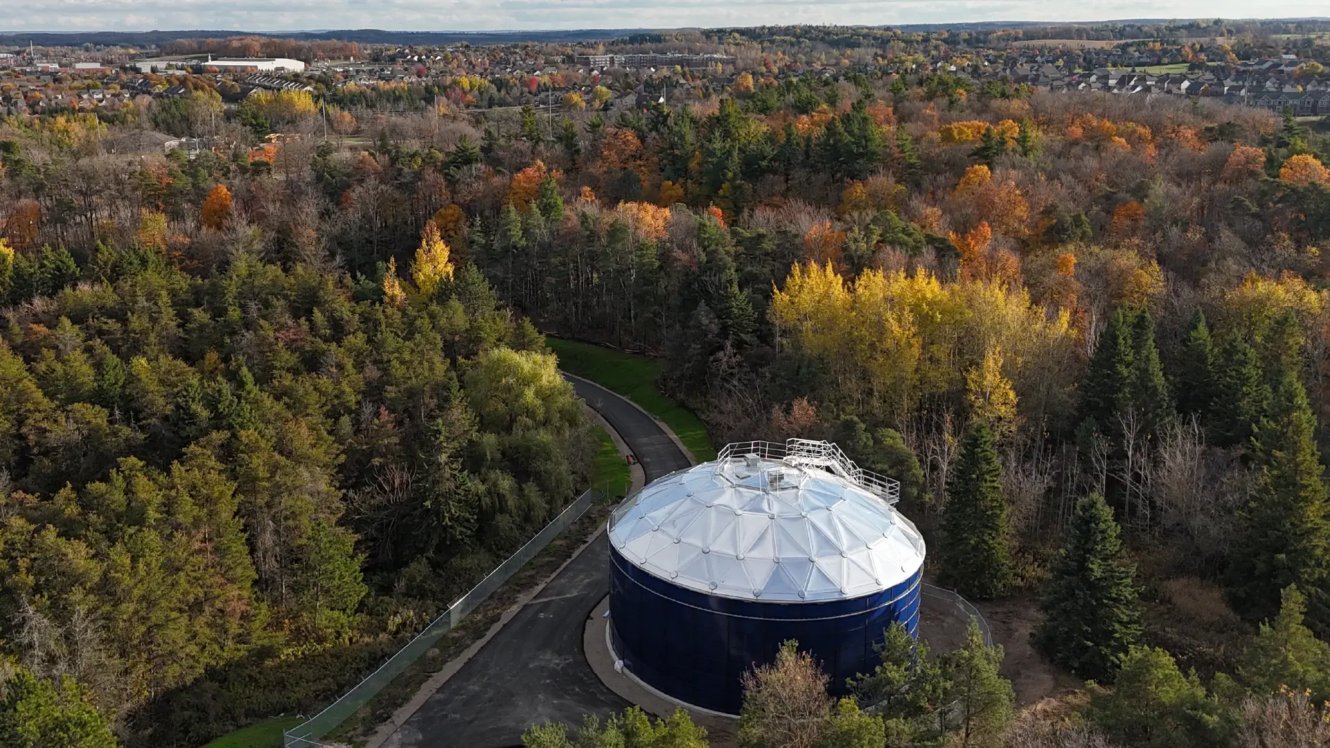 A Greatario built water tower sits in the foreground surrounded by autumn trees, in the distance is a small town. A Greatario built water tower sits in the foreground surrounded by autumn trees, in the distance is a small town.